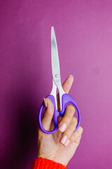Woman's hand in red sweater holds scissors on purple background