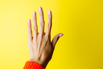 Woman's hand in red sweater shows five with fingers on yellow background