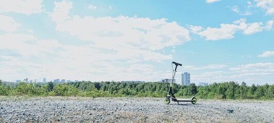 The scooter stands in the middle of the road behind it is a green horizon with a blue sky and white clouds. © NADEZHDA
