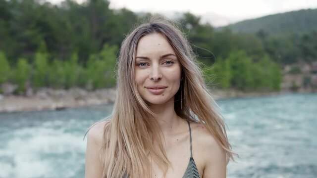 Carefree woman standing in front camera - green hills and river on background