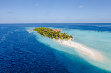 Fototapeta na wymiar Aerial view of the Maldivian island with wooden houses on a shallow water of a reef in the Indian Ocean