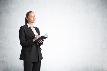 Woman writing in notebook standing on grey background, mockup empty wall