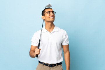 African American man over isolated blue background playing golf and looking up while smiling