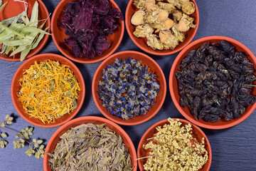 Different types of tea and herbs are in different clay bowls and are photographed from above