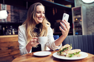 Happy mid adult woman using mobile phone at cafe having lunch