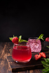 Refreshing strawberry lemonade with mint leaves, fruit water on a dark wooden background, summer drinks concept.