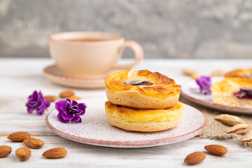 Small cheesecakes with jam and almonds with cup of coffee on a white wooden background. Side view, selective focus.