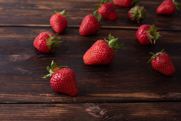 Ripe strawberries sprinkled on a dark wooden table, summer concept.