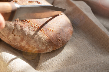 Сutting a fresh rye loaf with a knife close-up in sun glare