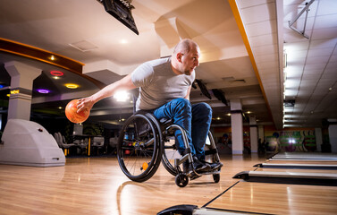 Young disabled man in wheelchair playing bowling in the club