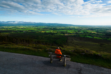 A man sits on a bench near the edge of the road admiring the views at Vee Pass, a v-shaped turn on the road leading to a gap in the Knockmealdown mountains in Clogheen county Tipperary, Ireland