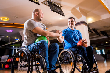 Two young disabled men in wheelchairs playing bowling in the club