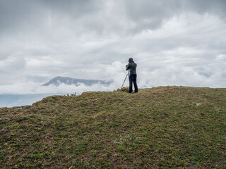 Rear view of hiker photographing sea through SLR camera while standing on a cliff in difficult weather conditions.