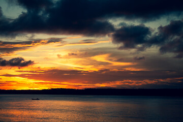 Fototapeta premium Fine art photography of a vibrantly colored sunset on the lagoon. Small silhouette of a boat.