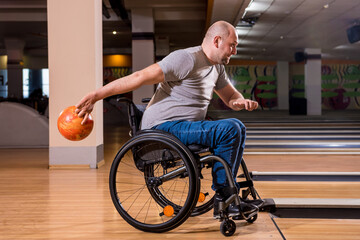 Young disabled man in wheelchair playing bowling in the club