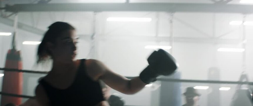 HANDHELD Spectators gather around ring to watch boxing sparring match between male and female fighters inside a gym. Shot with 2x anamorphic lens