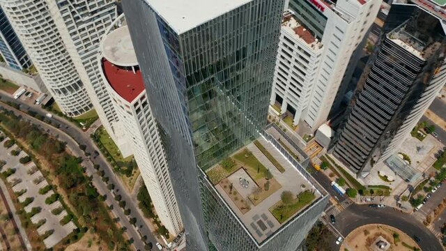 High angle view of tall modern glass cover building. Drone camera flying around Paradox Torre skyscraper, tilting up to show cityscape. Mexico city, Mexico.