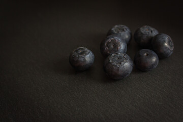 Blueberries on black cutting board. Forest berries on the table with vignette. Blueberries isolated. Summer harvest. Vitamin and antioxidant concept. Juicy dessert. Fresh ripe berries. Organic food. 