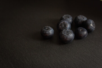 Blueberries on black cutting board. Forest berries on the table with vignette. Blueberries isolated. Summer harvest. Vitamin and antioxidant concept. Juicy dessert. Fresh ripe berries. Organic food. 