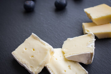 Brie cheese and blueberry on black cutting board. Camembert cheese slices with berries on black background, top view. Healthy food concept. Cheese and berries on black plate with copy space.