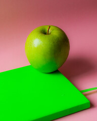 swooping shot of a green apple on a green notebook on a pink background