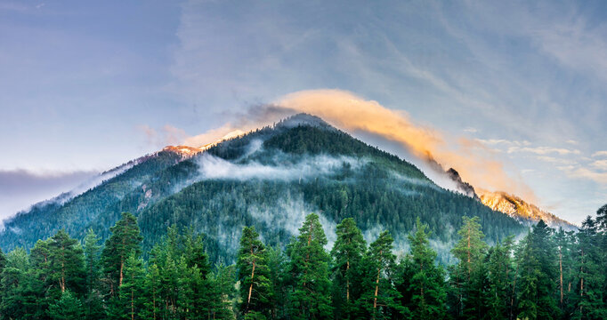 Panoramic landscape view, snow covered mountain peaks and colorful clouds over mountain range during sunset, Arkhyz villadge, Caucasus mountains, Russia