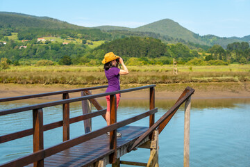Fototapeta na wymiar A young tourist looking at birds with spyglasses from the wooden piers of the Urdaibai marshes, a biosphere reserve in Bizkaia next to Mundaka. Basque Country