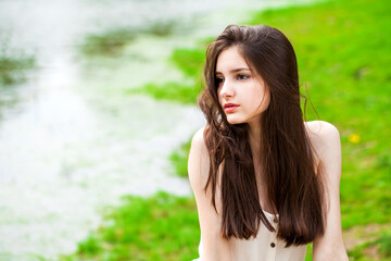Portrait of a young beautiful brunette girl posing in summer park