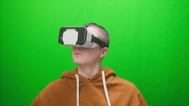 Close-up of young man wearing virtual reality glasses, playing vr video games. Student enjoying AR 3D video games on green background, modern console, next gen 2020, new era of consoles. 