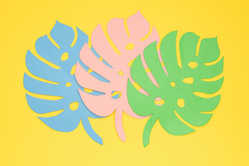 Three paper-cut multi-colored monstera leaves on a yellow background. Summertime Exotic tropical concept.