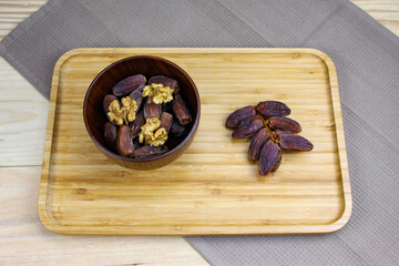 Obraz na płótnie Canvas Twig with dates on a wooden tray. Wooden bowl with dates and walnut kernels. Fruit on a wooden tray. Fruit dates. Walnut kernels.