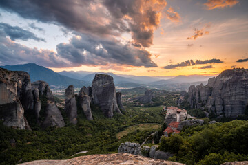 Fototapeta na wymiar Scenic sunset landscape of a wide mountain valley in Greece with bizarre cliffs, a dense forest at the foot of the mountains, and a small Christian monastery on top of a cliff