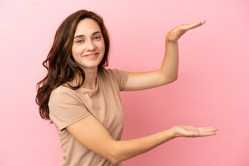 Young caucasian woman isolated on pink background holding copyspace to insert an ad