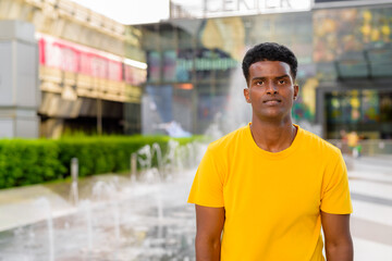 Portrait of handsome black African man wearing yellow t-shirt outdoors in city during summer next to fountain