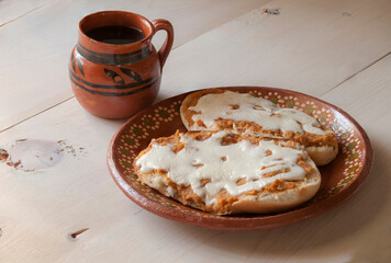 Molletes on a mexican mud plate and black coffee in a mexican mud cup on a wooden table, as part of Mexico traditional breakfast.