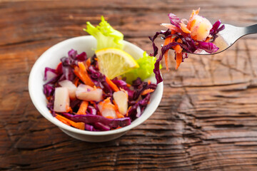 Fork with salad in a female hand over a plate of cole slow salad on a wooden background.