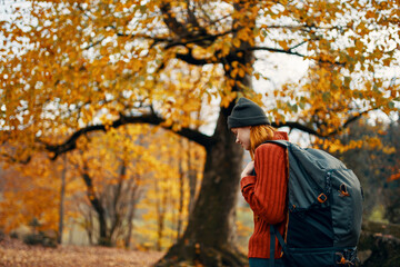 woman in a sweater cap with a backpack on nature in the forest landscape and fallen leaves