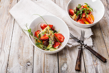 Delicious summer salad. Salad with fresh strawberries, baked beets, yellow tomatoes, dor blue cheese and herbs in a white bowl on a light rustic background. Top view. Copy space. Summerfood