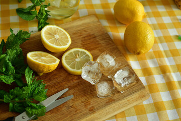 Fresh ripe lemons, peper mint and ice cubes on cutting board on wooden background. lemonade sassy water.Summer mood