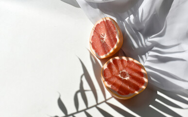 Close up summer still life flat lay with two cut grapefruits and white silk fabric on table in...