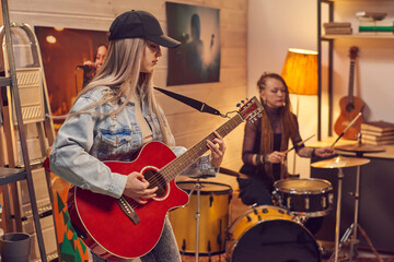 Fototapeta premium Female musicians playing guitar and drum in modern studio
