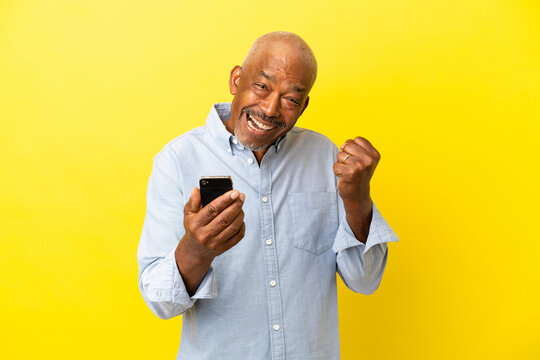 Cuban Senior isolated on yellow background with phone in victory position