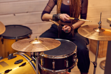 Fototapeta na wymiar Drum set and young female with drumsticks sitting near by