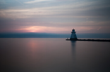 Simple and clean landscape shot of the ocean horizon and and a lighthouse during a beautiful orange/red sunset in Port Elgin, Ontario, Canada.