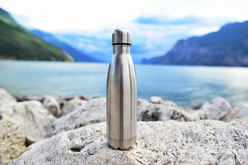 Close-up of steel eco thermo water bottle on the background of the lake in the mountains. Be...