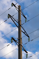 Concrete tower of power lines against the background of a blue sky with clouds