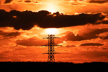 Silhouette of the lattice power tower against the background of the evening red sky