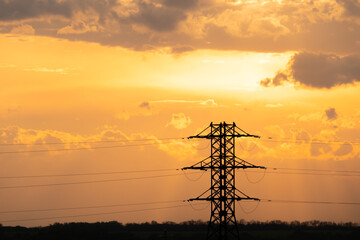 Silhouette of the lattice power tower against the background of the evening yellow sky