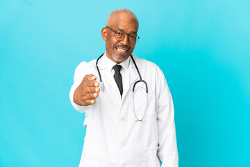 Senior doctor man isolated on blue background shaking hands for closing a good deal