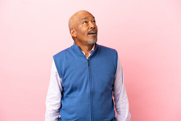 Cuban senior isolated on pink background looking up and with surprised expression